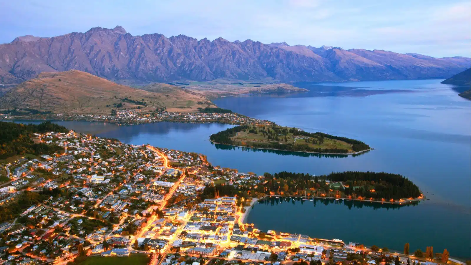A panoramic view of Queenstown in New Zealand at dusk. When looking at a New Zealand map, Queenstown is located in the Otago region of South Island.