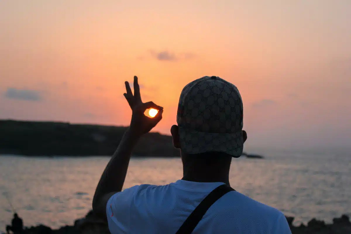 Man making an "okay" sign with his fingers over a setting sun.